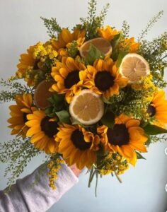 Görseldeki buket, enerjisi yüksek ayçiçekleri (günebakan), taze limon dilimleri ve minik sarı çiçekli dolgu bitkileriyle (Solidago/Altınbaşak) hazırlanmış, alışılmışın dışında, modern ve ferah bir aranjmandır. Bu tarz bir ürün için "yaz enerjisi" ve "sıra dışı tasarım" vurgusu yapmalısınız.