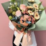 Görseldeki buket; şeftali tonlarında gerberalar, pudra pembesi güller, egzotik agapanthus (mavi/beyaz leylak) ve minik krizantemlerin soft yeşil bir ambalajla birleştiği, oldukça modern ve "bohem" bir tasarımdır.