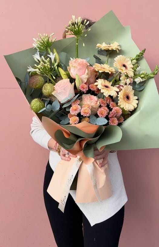 Görseldeki buket; şeftali tonlarında gerberalar, pudra pembesi güller, egzotik agapanthus (mavi/beyaz leylak) ve minik krizantemlerin soft yeşil bir ambalajla birleştiği, oldukça modern ve "bohem" bir tasarımdır.