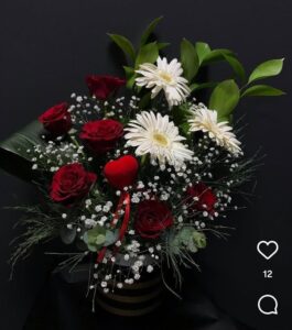 Görseldeki ürün; siyah-gold çizgili silindir kutu içerisinde kırmızı güller, beyaz gerberalar, bolca cipso (gelin nefesi) ve ortasında romantik bir kadife kalp figürü barındıran, kontrastı yüksek ve oldukça şık bir kutu aranjmanıdır.